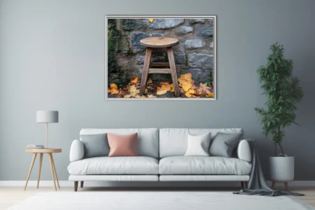 Rustic wooden stool with autumn leaves against aged stone wall, warm earthy tones