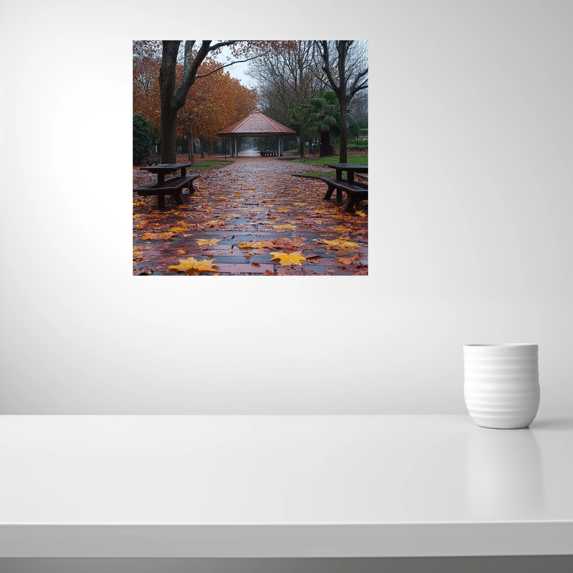 Rainy autumn park path with fallen leaves, picnic tables, and a gazebo in muted amber and grey