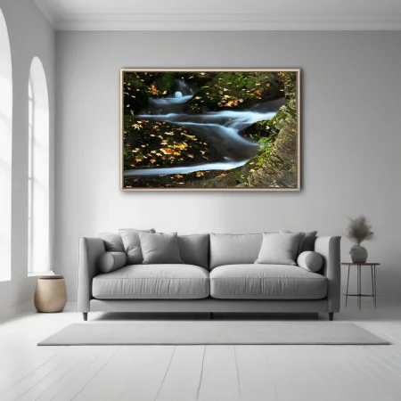 Long-exposure mountain stream with autumn leaves on mossy rocks, blue-white silky water