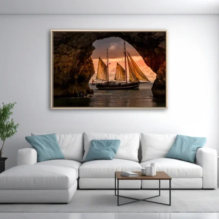 Tall ship with golden sails framed by sea arch at sunset